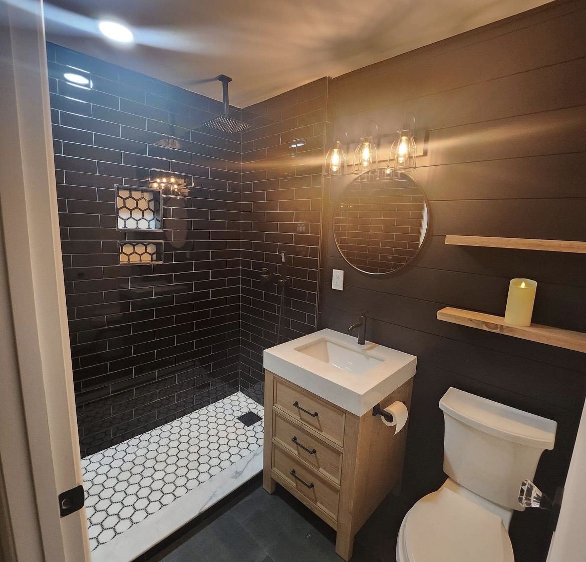Guest bath with dark subway tile shower, hexagon marble floor, lighted niches, floating shelves and a rustic wood vanity.