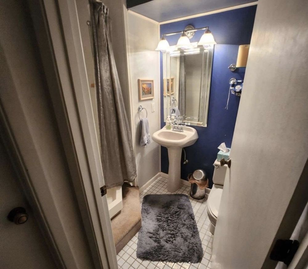 Dated bathroom before renovation: pedestal sink, small white floor tile and a curtained shower.