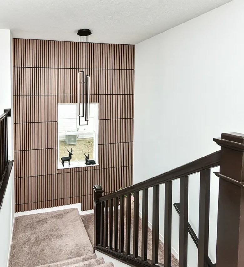 Two-story stairwell with a walnut wood slat accent wall and a modern linear pendant light.